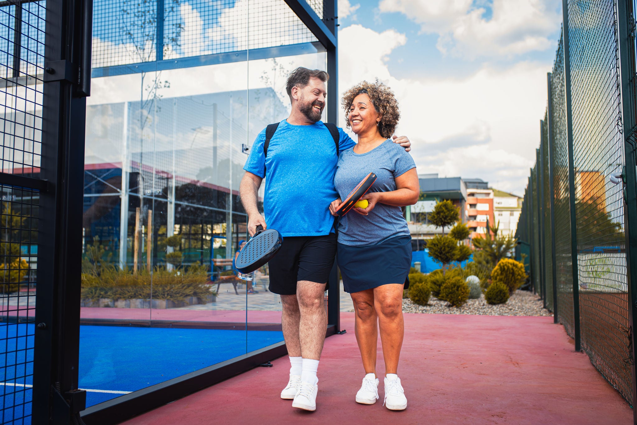 Smiling couple comes to the outdoor court to play padel.