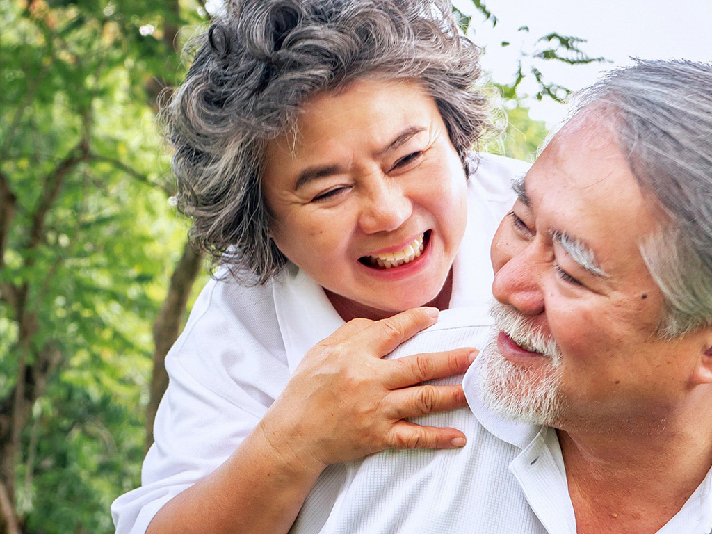 An elderly couple laughing together outside.