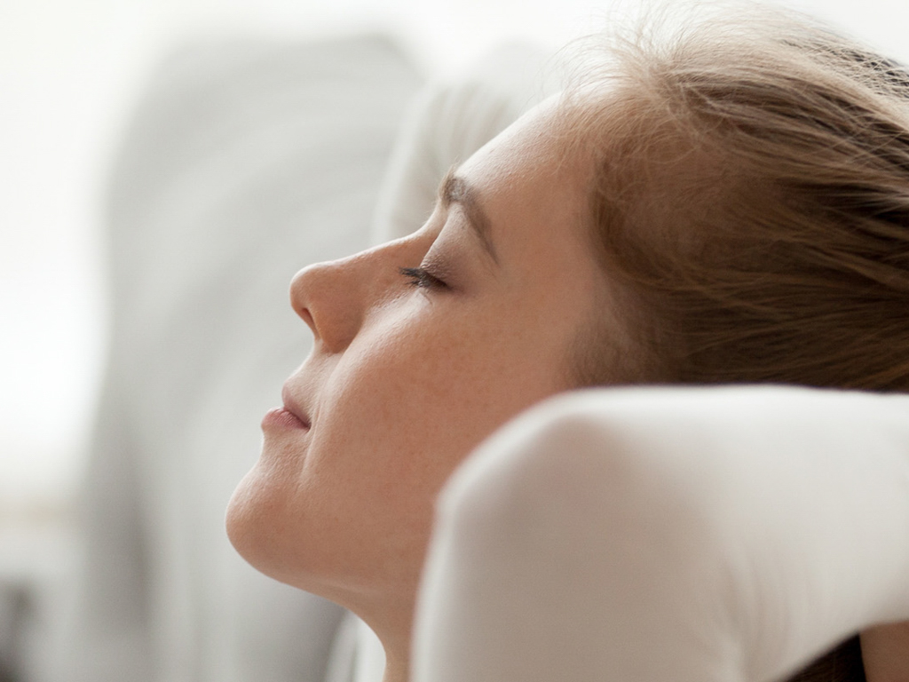 A young child is seen reclining on a white sofa in a softly lit, modern interior. The setting appears calm and comfortable, with neutral tones and minimal distractions in the background. The child's light brown hair is visible, and the overall mood is peaceful and relaxed. No visible text or numbers are present in the image.