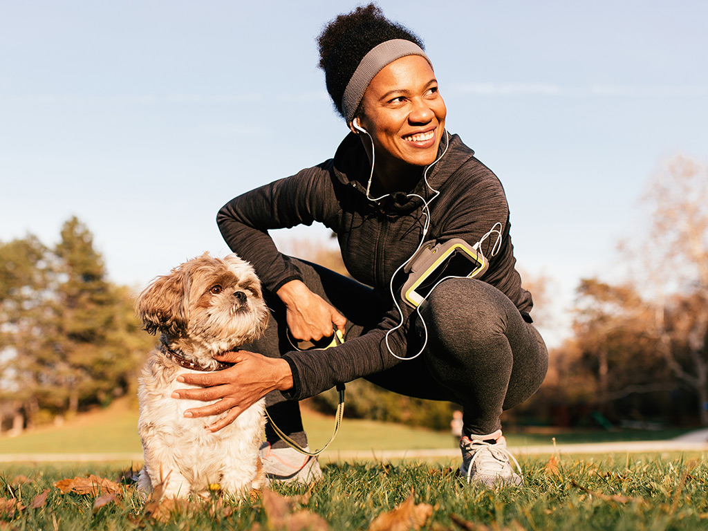a woman in running gear squats down to pet her dog