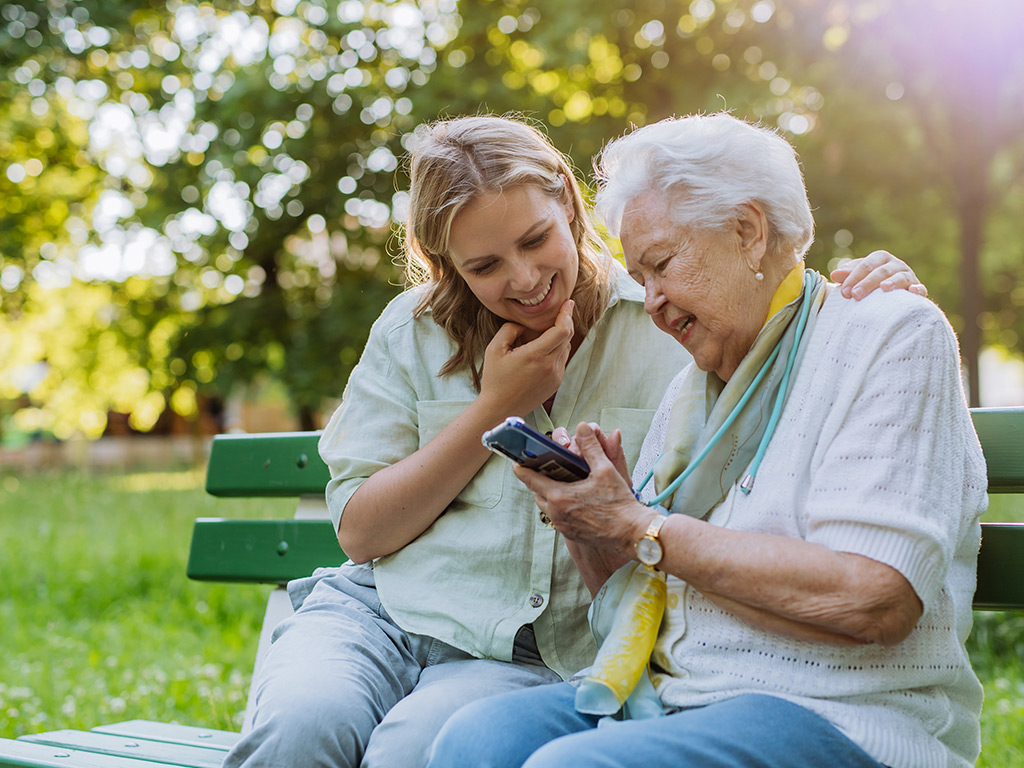 An elderly woman shows a a younger woman her phone screen.