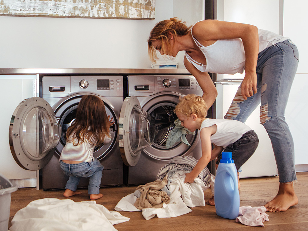 Mother and two young children doing laundry.