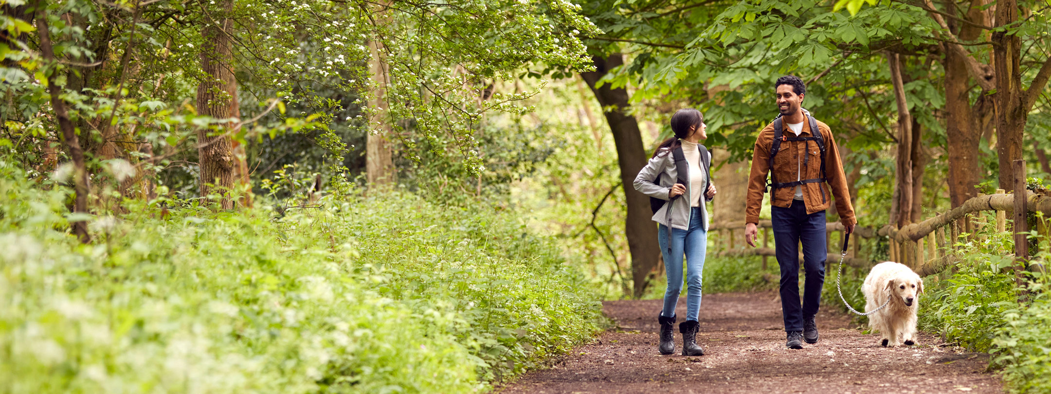 A young couple walks on an outdoor trail with their dog
