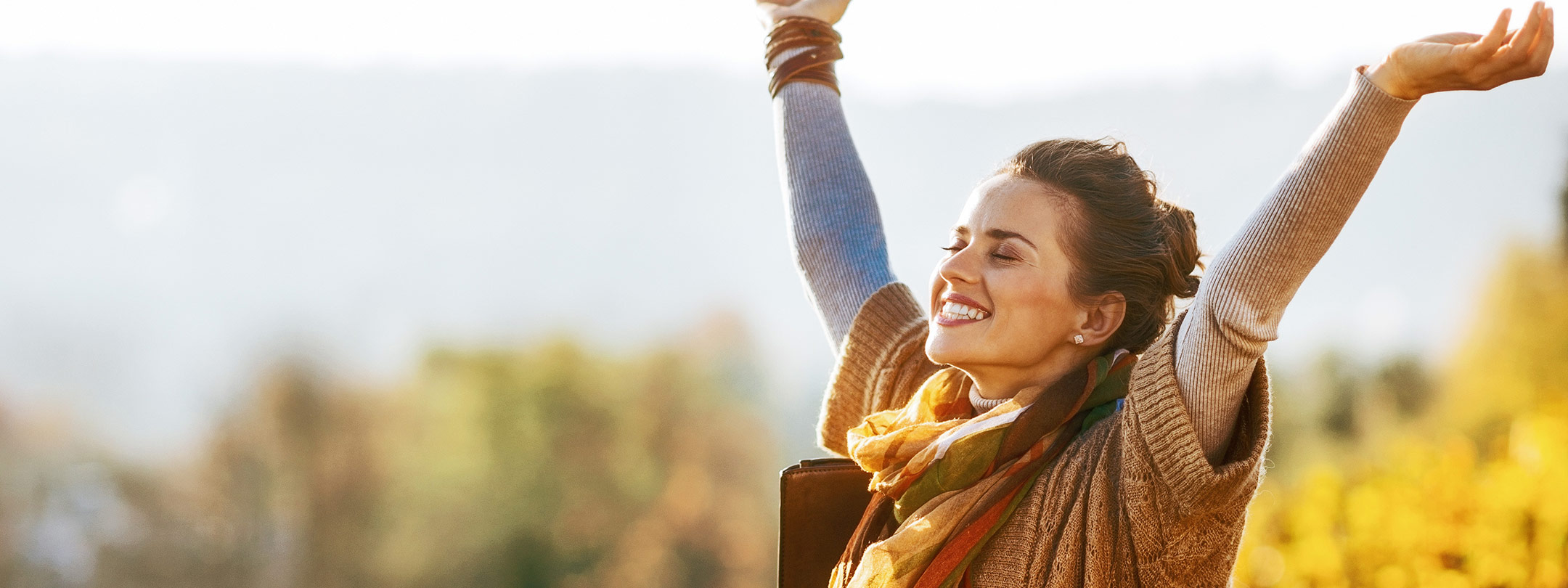 A happy woman throws her arms in the air smiling outside