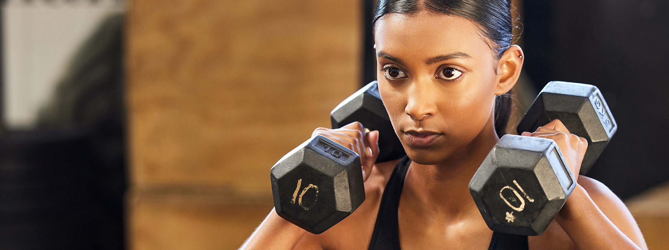 A young woman is lifting dumbbells above her shoulders
