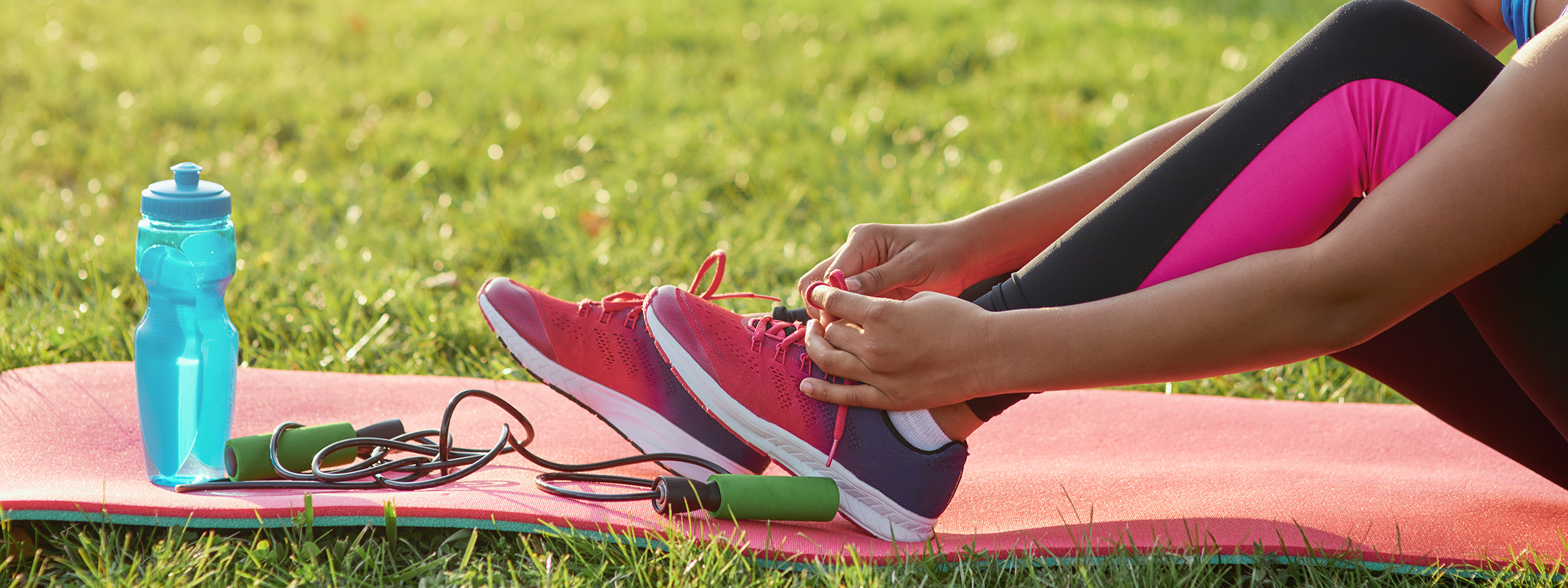 A woman ties her sneakers on an exercise mat outside