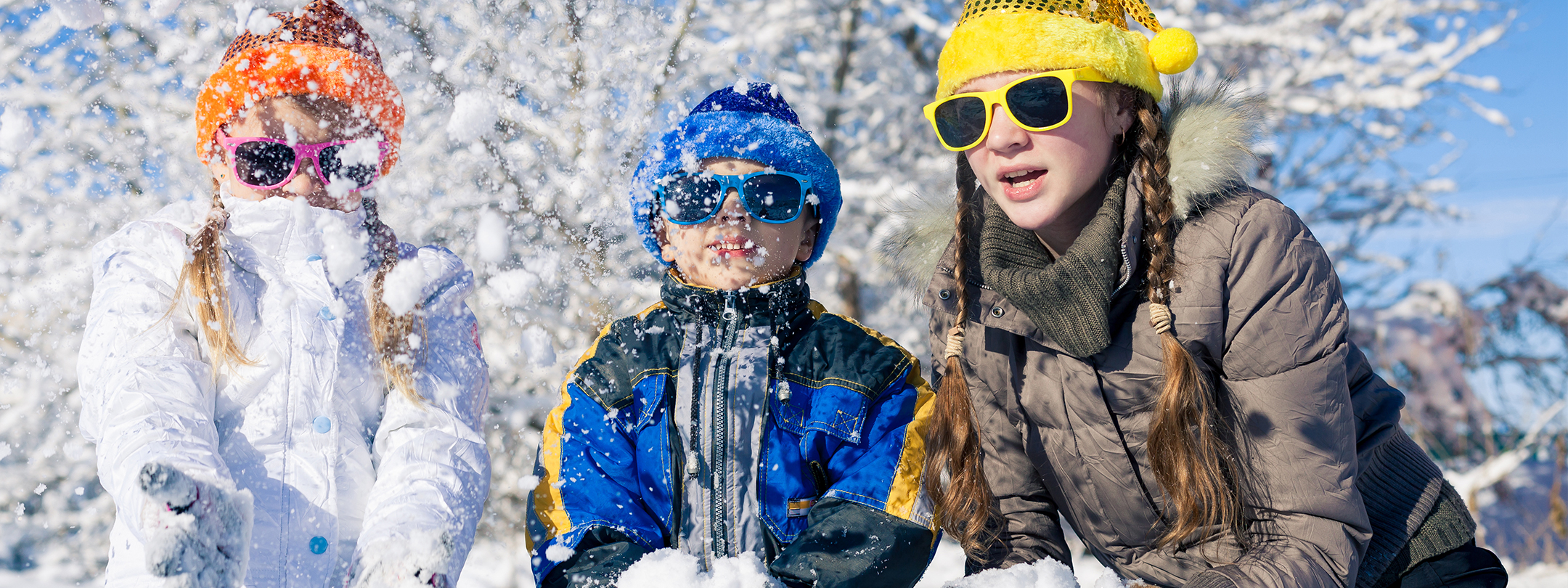 Kids throw snow in the air playfully on a sunny day.