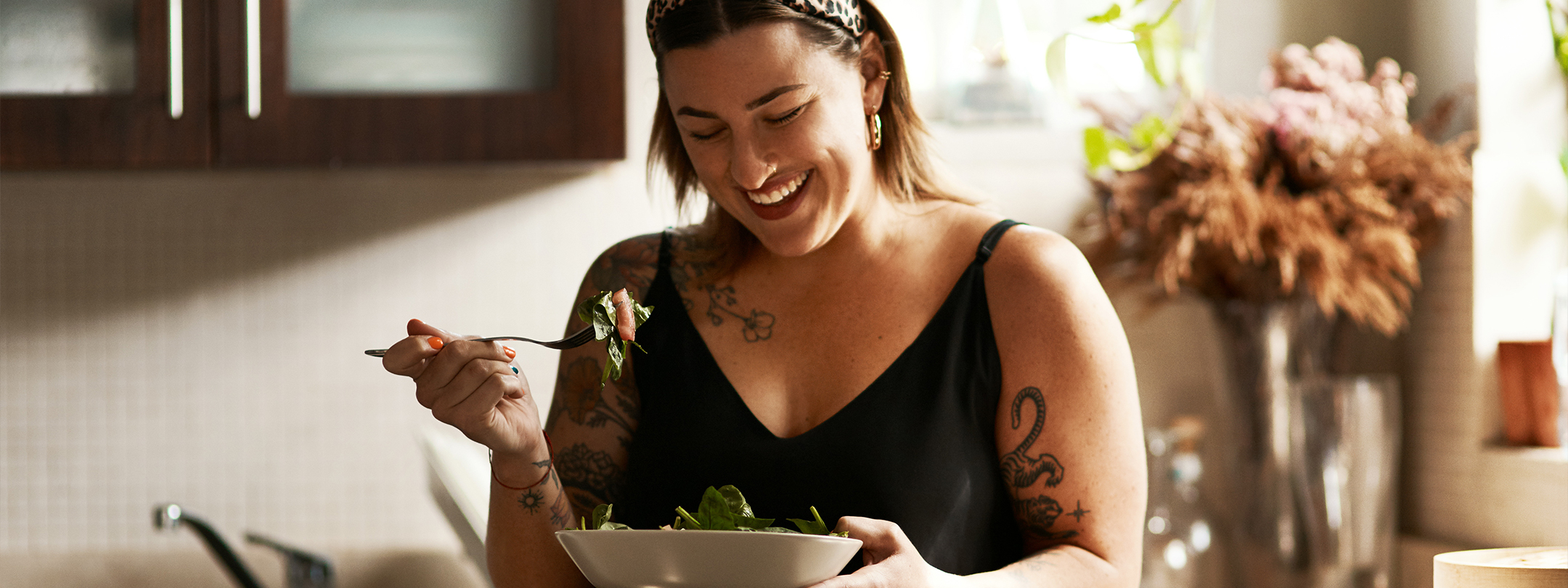 Woman in kitchen is smiling and eating a salad