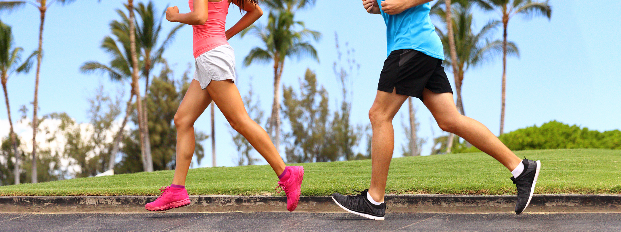 A man and woman are jogging outside near palm trees and grass