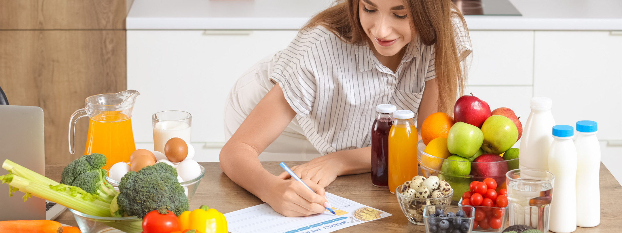 A smiling woman meal plans with healthy food on the counter