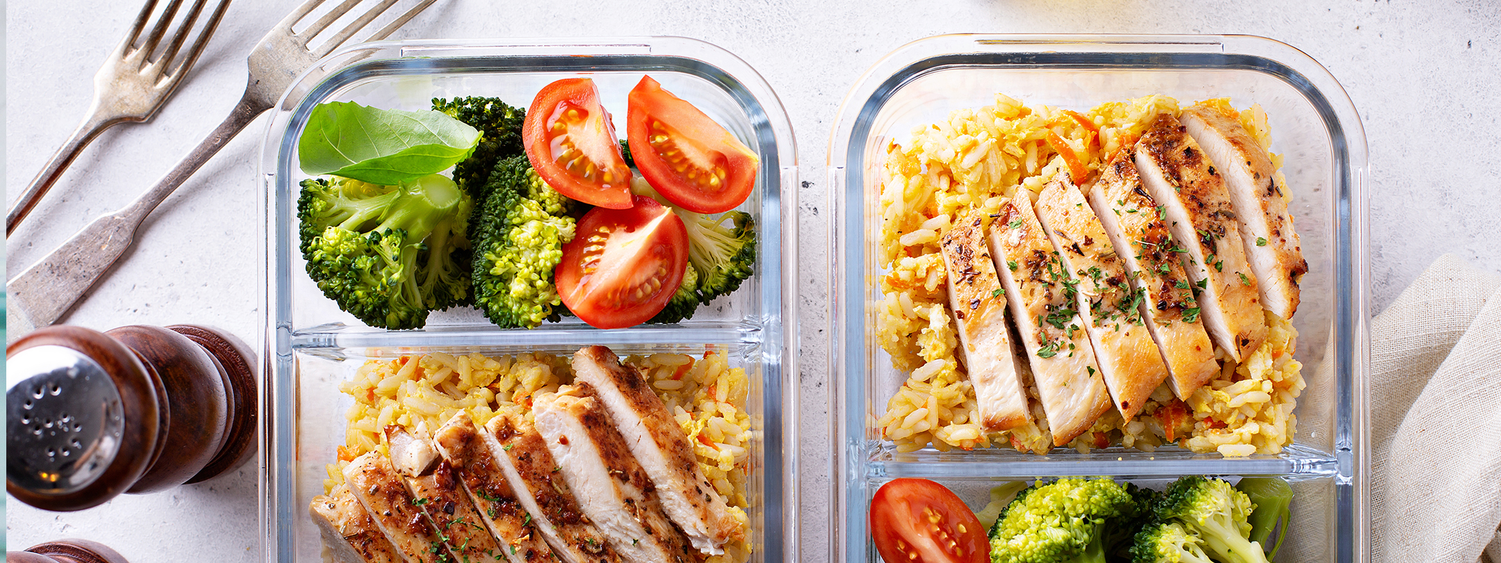Two meal prep containers with healthy foods including chicken, rice, and vegetables