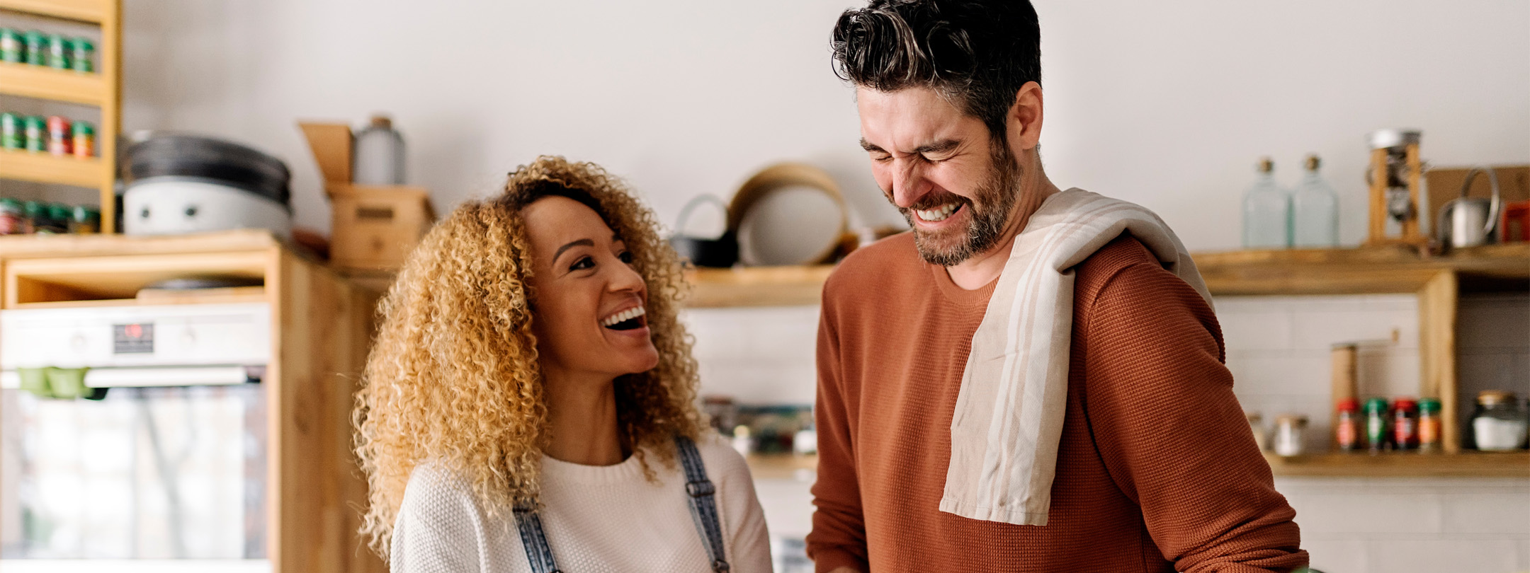 A man and woman laugh while cooking in a kitchen