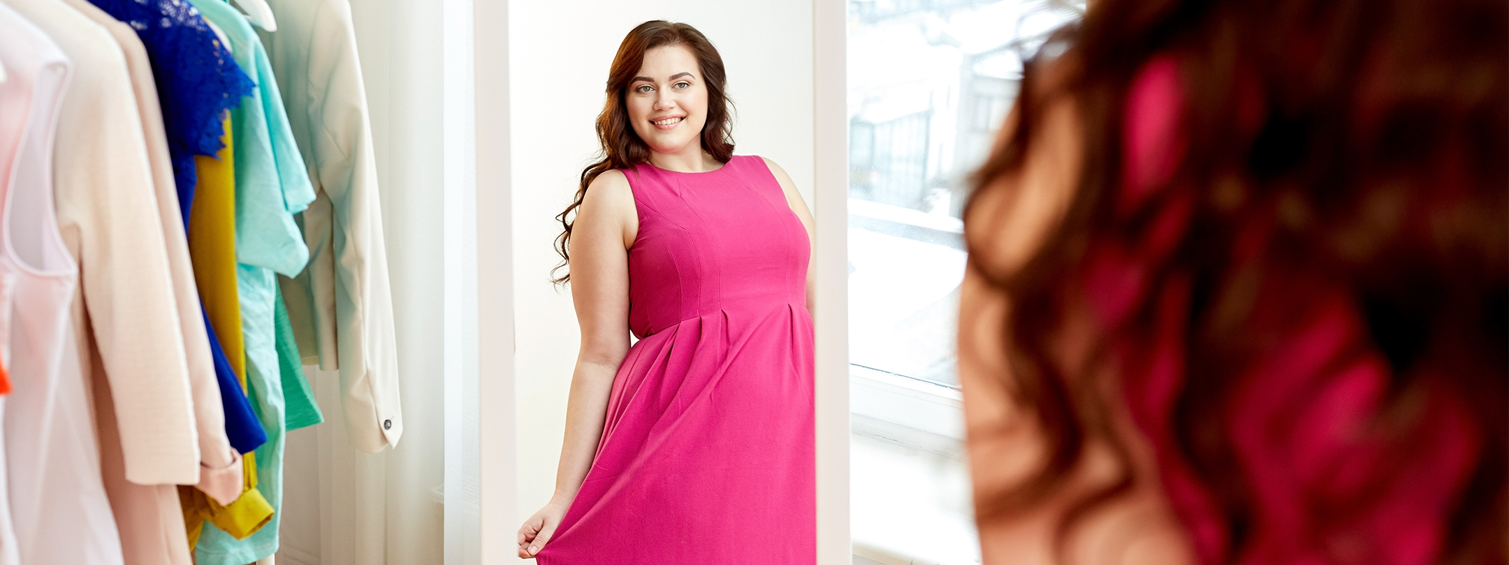 A happy woman smiles at her reflection in the closet mirror