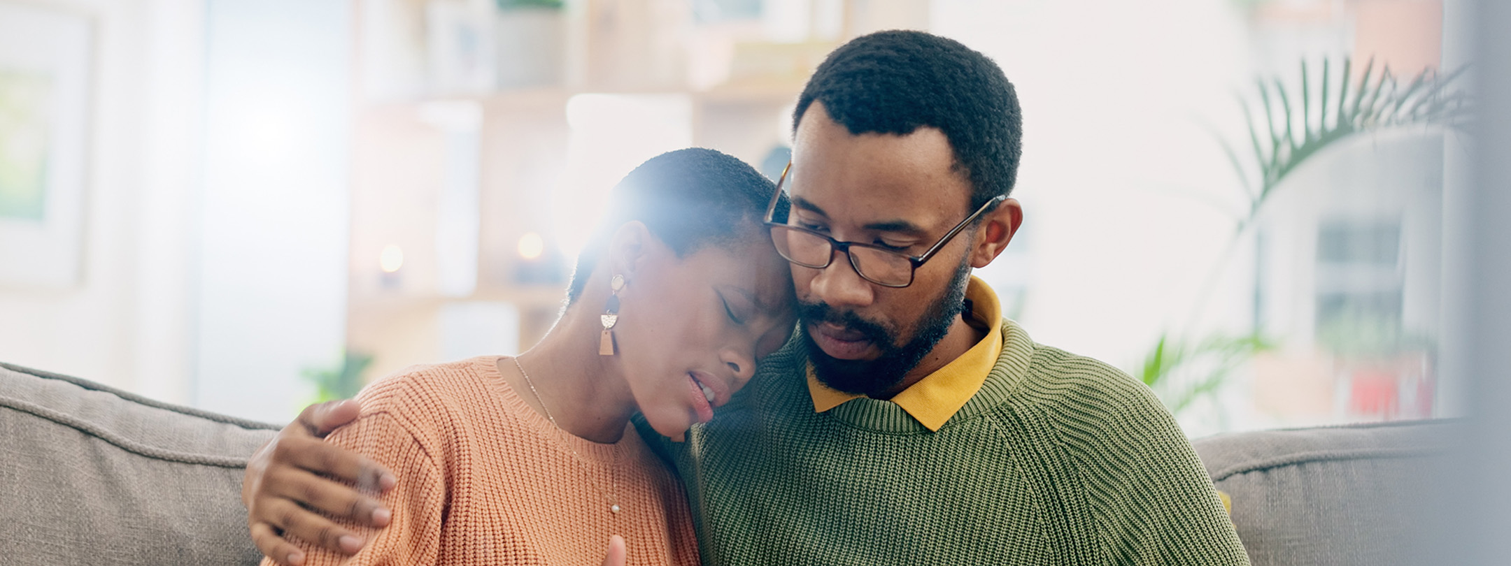 A sad woman is comforted by a man while sitting on a couch
