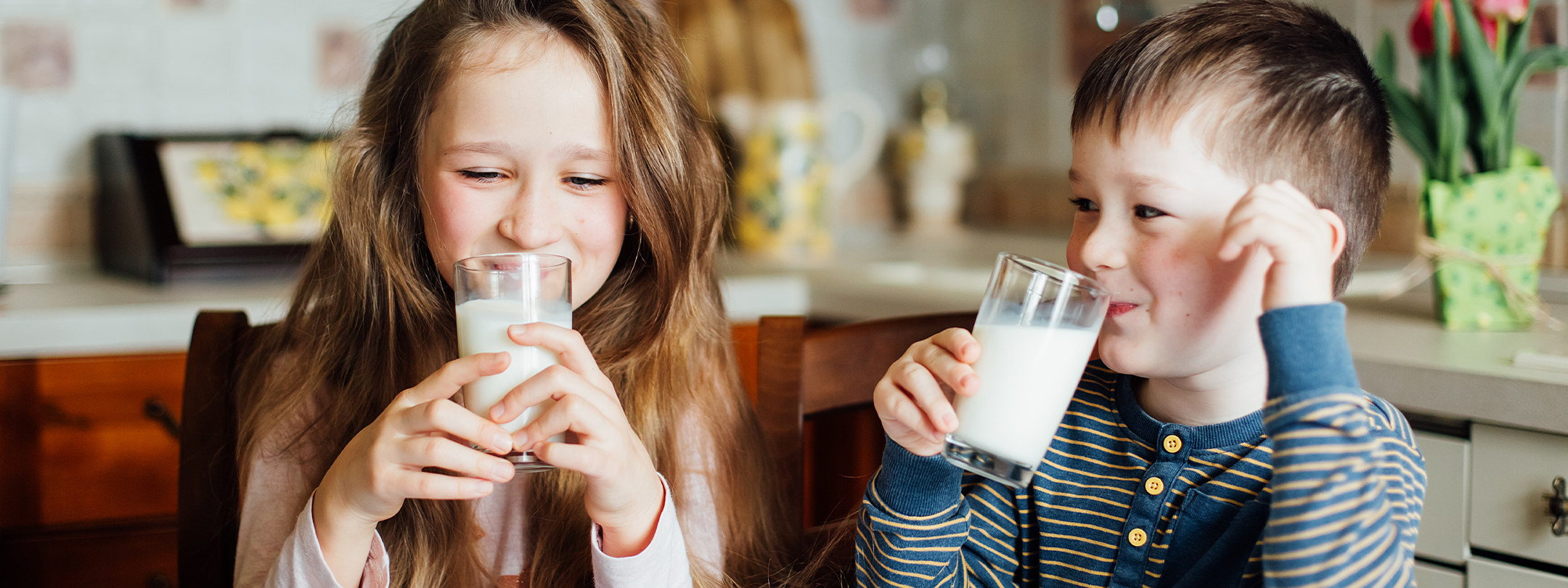 A young boy and girl drink milk in a kitchen together