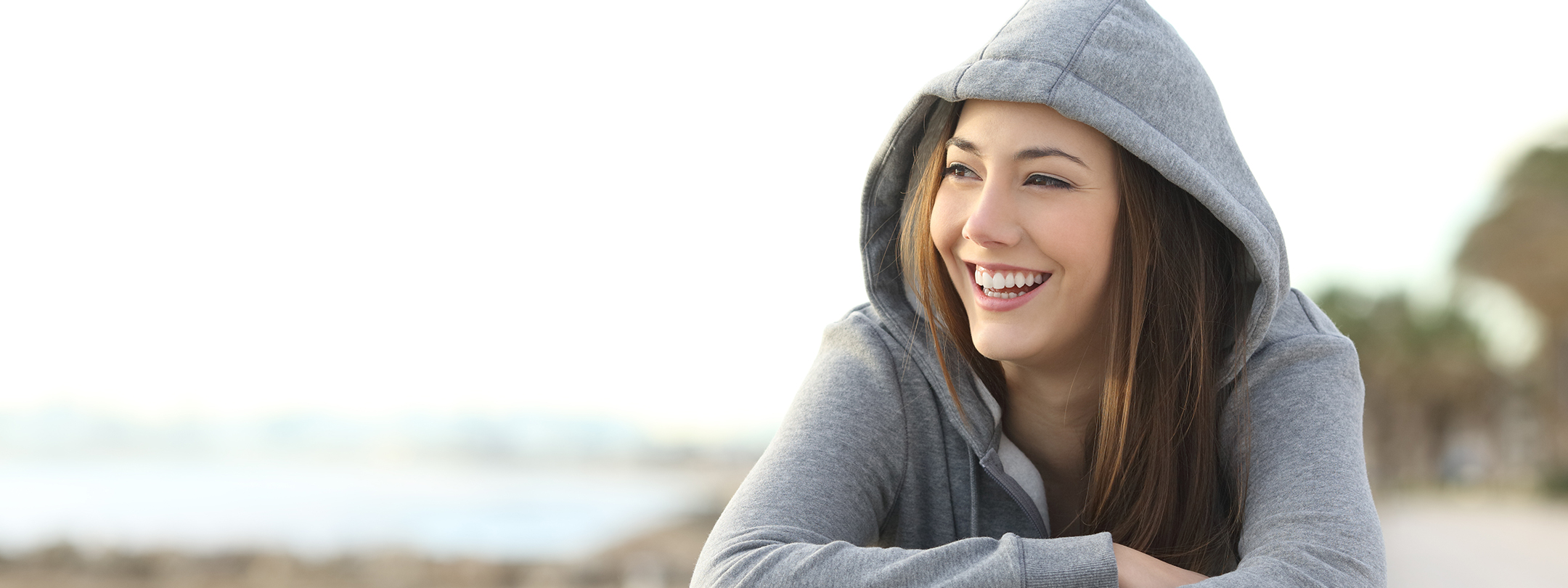 A young woman wearing a sweatshirt hood smiles outside