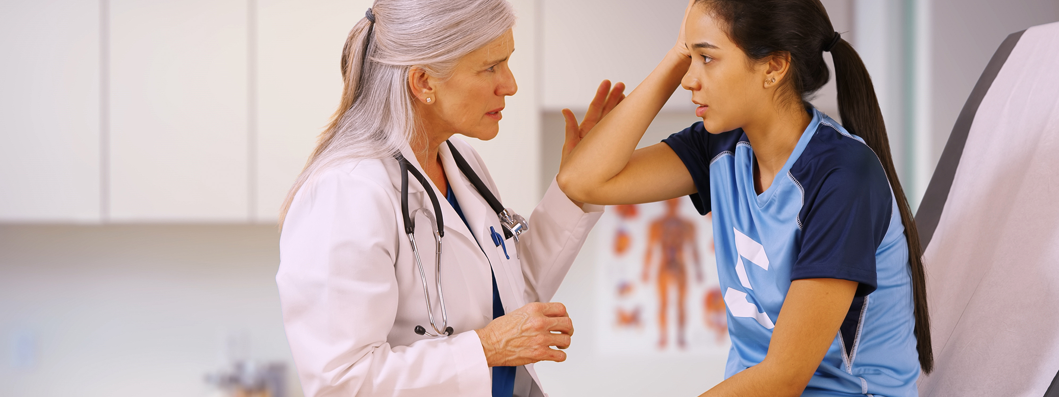 A female doctor speaks to female teenage patient as she shows a painful spot on head