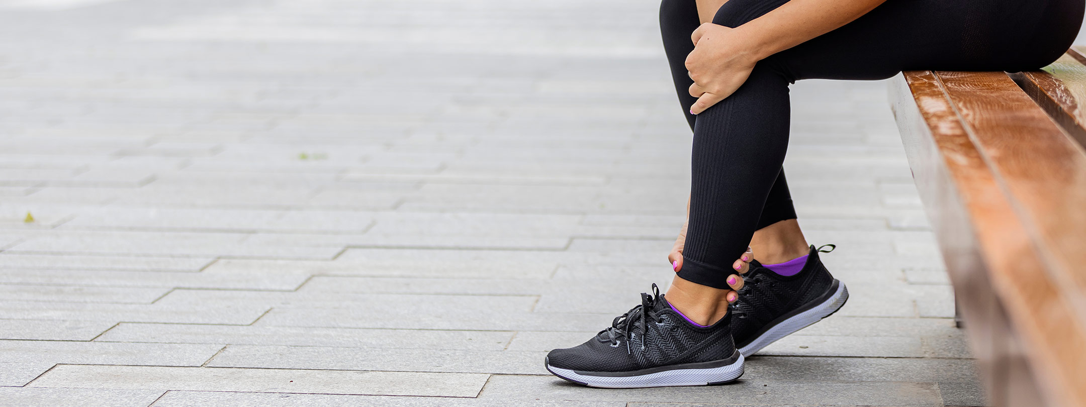 a woman in exercise gear holds ankle and knee in pain