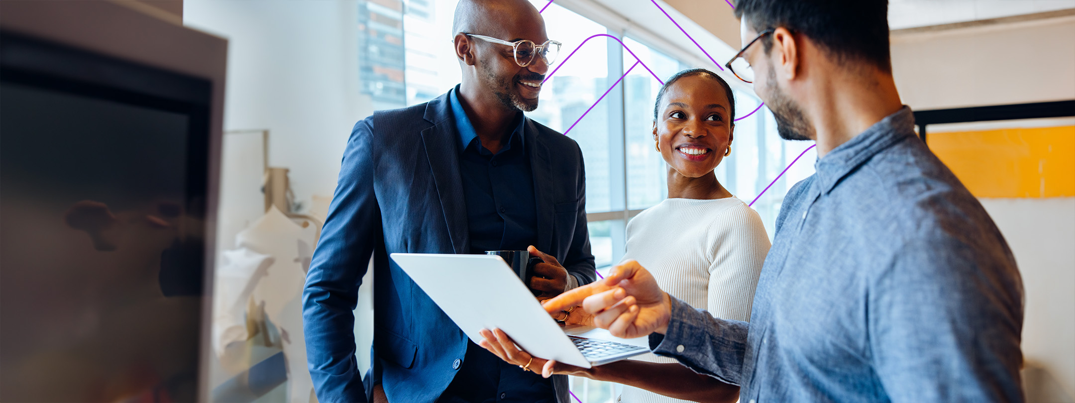 A group of three team members reviewing a laptop in an office setting.