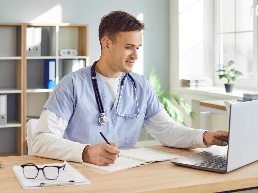 Medical provider writing while using a laptop computer