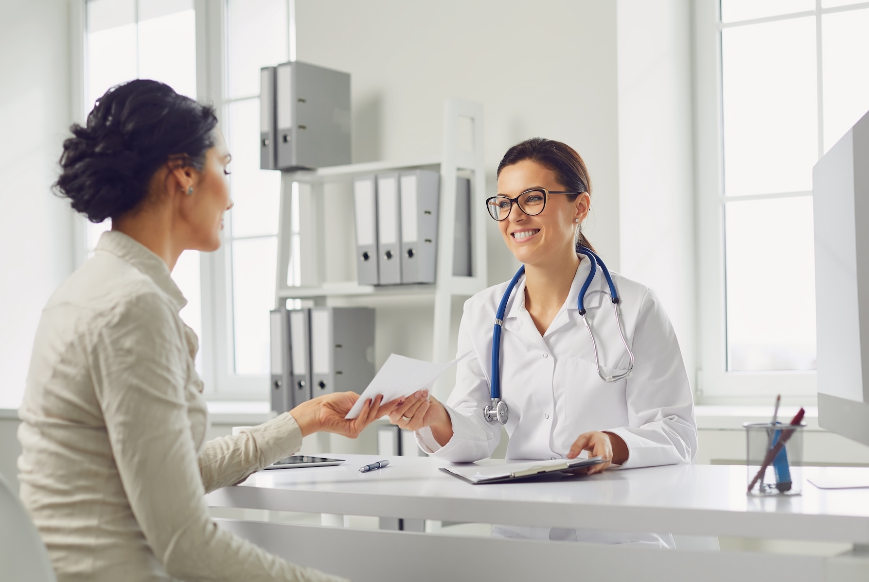Smiling female patient at consultation with woman doctor sitting at table in office clinic.. Medicine clinic hospital.