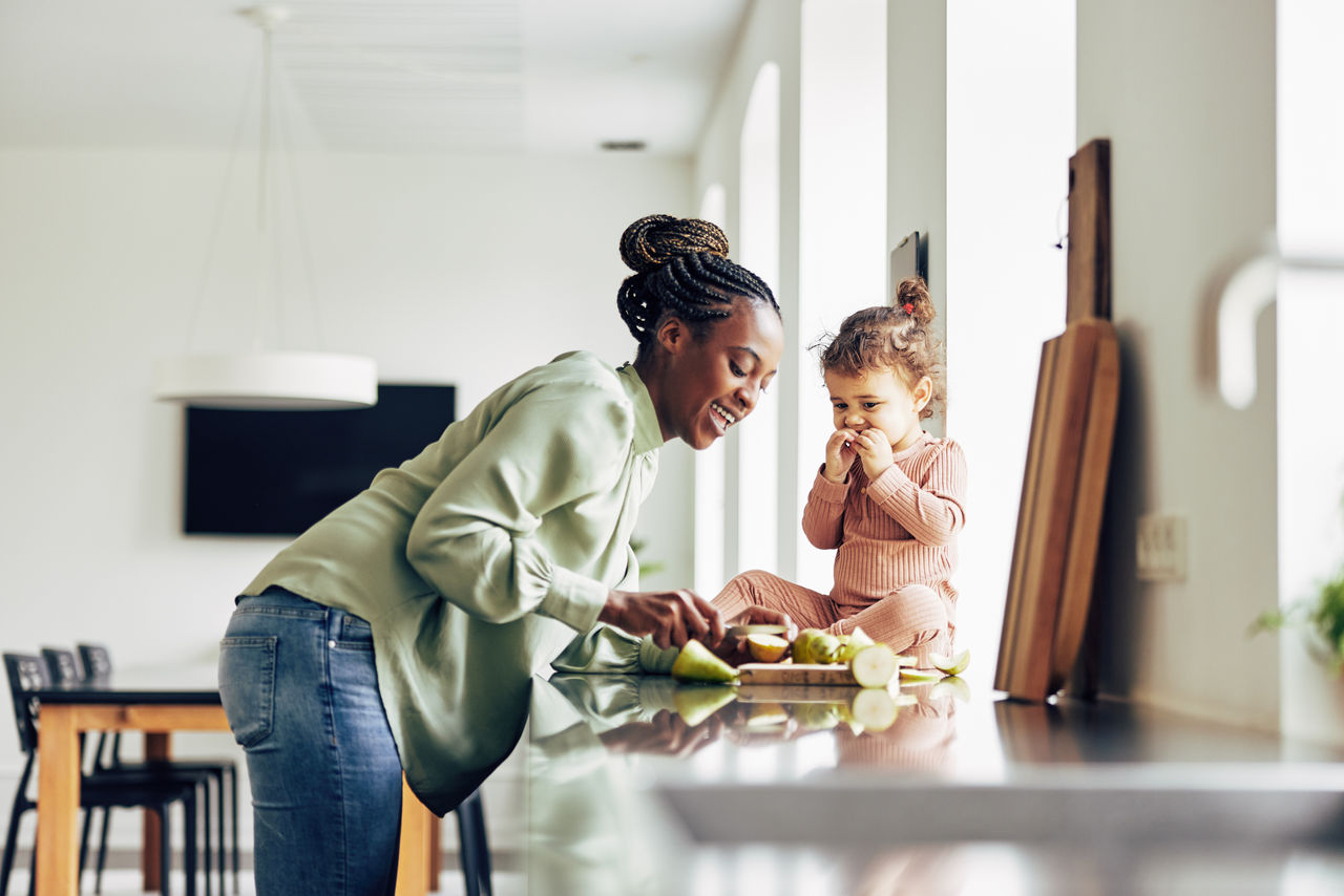 Smiling young African mom and her adorable little girl enjoying a healthy fruit snack together in their kitchen at home