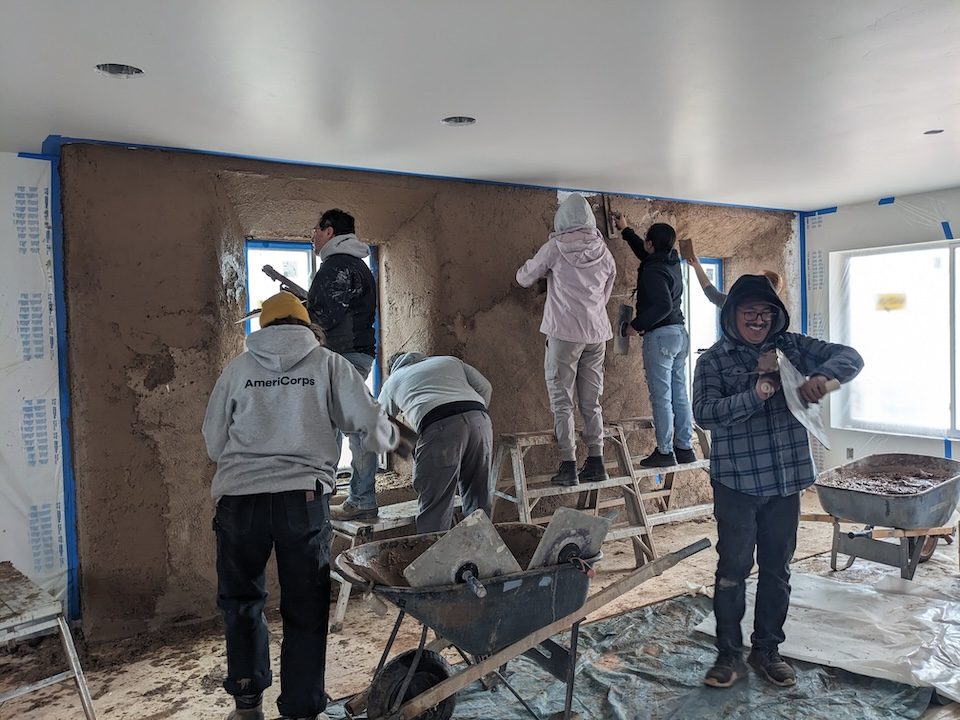 Equipo de trabajadores de construcción voluntarios aplicando una mezcla de paneles de yeso a una pared